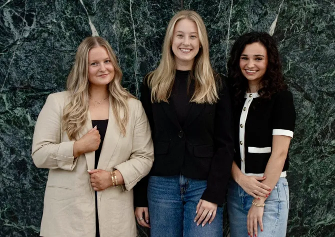 Three women standing in front of a green marble wall.