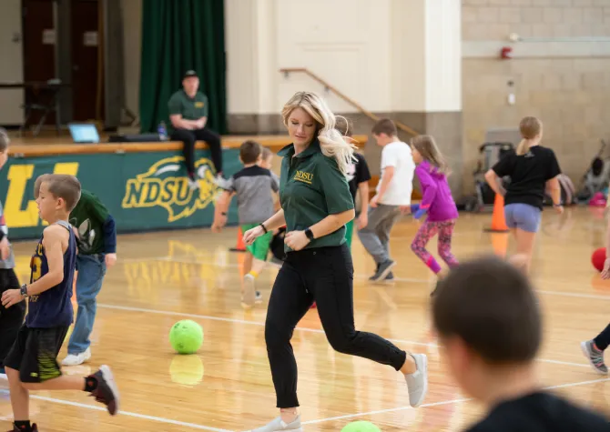 Student running through a gym while teaching a gym class with young students.