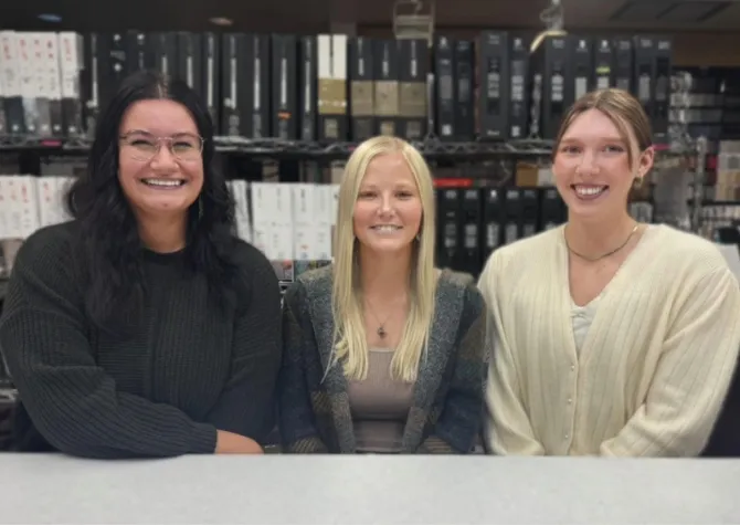 Three women sitting at table while smling confidently at camera.