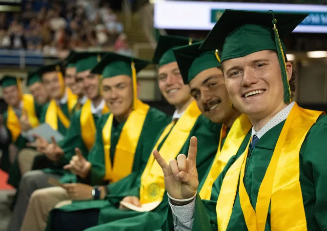 students smile for the camera and give the Bison horns hand signal at commencement 