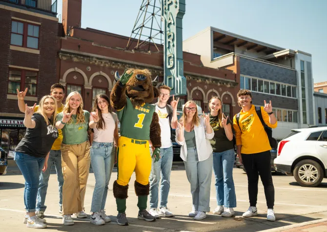 A group of NDSU students and mascot, Thundar, stand next to each other in front of the Fargo Theatre sign
