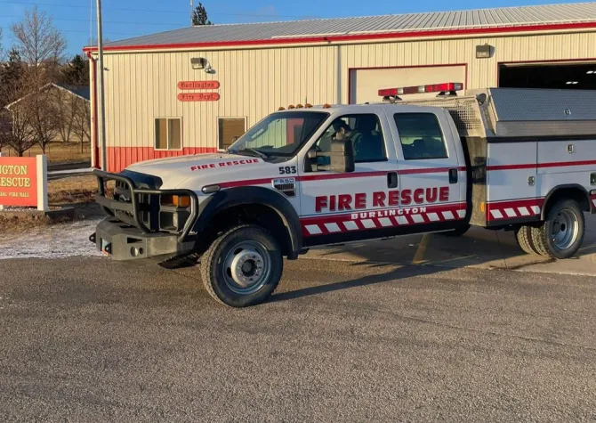 A wildland fire engine is parked outside a fire hall.