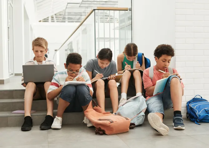 Students sitting on steps while working with laptop, pen and paper.