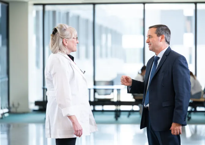 A man in a suit talks to a woman in a doctor's coat