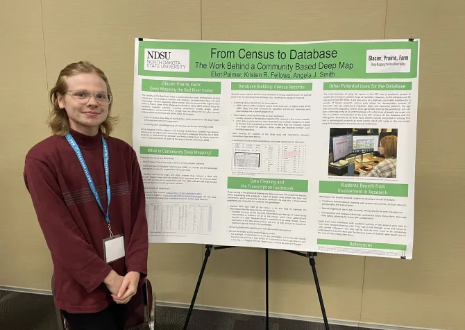 Student posing next to research poster while smiling at camera.