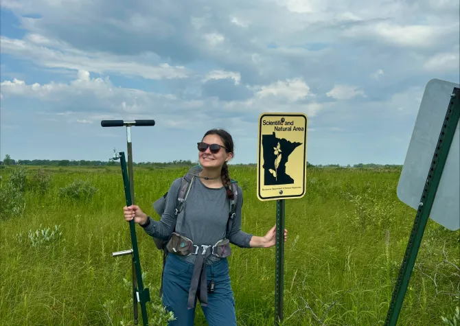 Josie Pickar standing in field holding equipment and sign.
