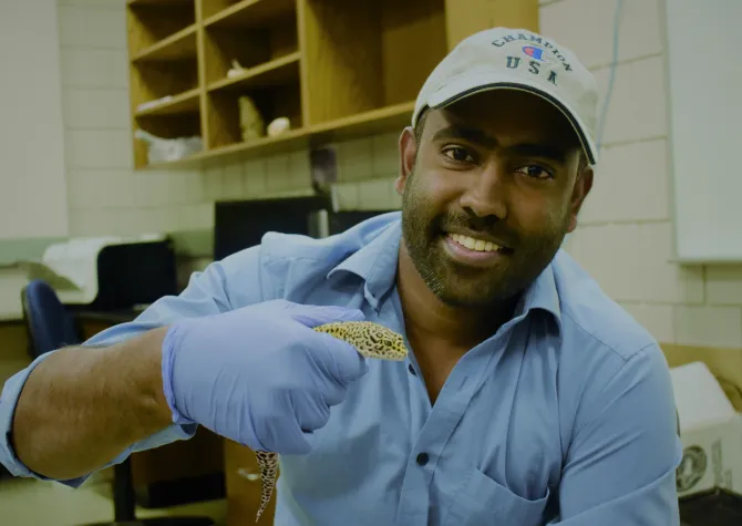 Sekhar smiling confidently at camera while holding an animal with blue gloves.