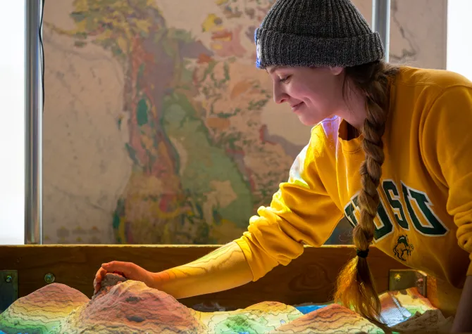 Student wearing a yellow NDSU sweatshirt working in AR sandbox.