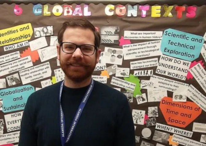 Mike Goulet standing in front of a bulletin board titled, 'Global Contexts'.