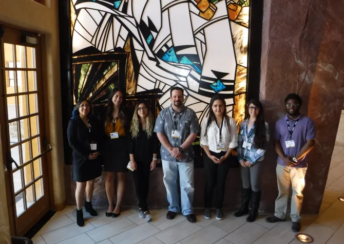 Students stand with faculty member while looking confidently at camera. 