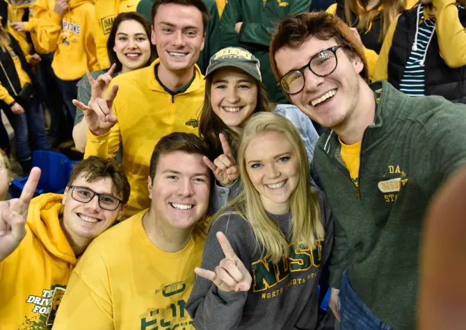 Students smiling confidently at camera showing the horns up sign with hands