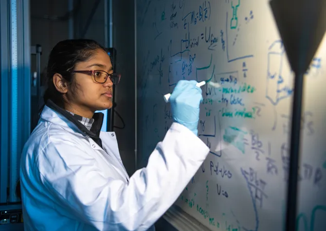 Research student working at a whiteboard. Looking intently at what she is current writing.