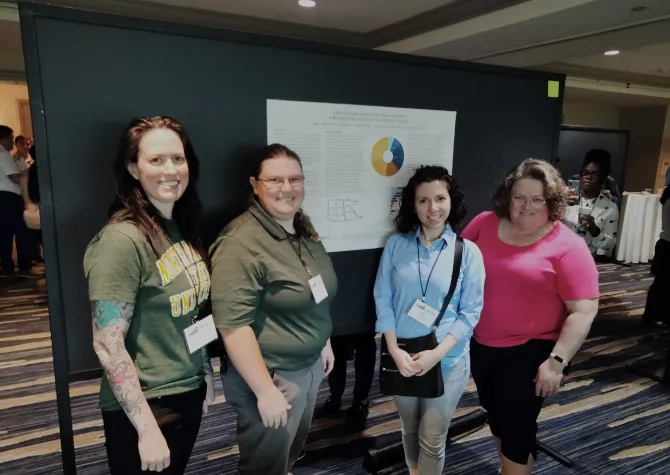 Team of researchers standing in front of research poster, smiling confidently at the camera