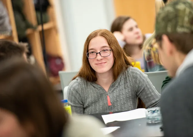 Student looking at another student sitting at the same table. 