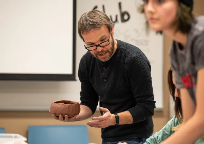 Faculty holding clay artifacts while teaching students in a classroom setting.