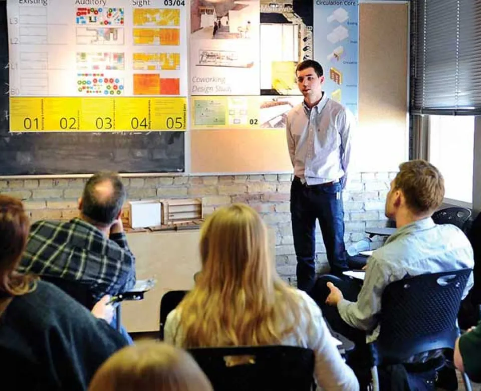 Student sitting in class listening to presenter at front of room.