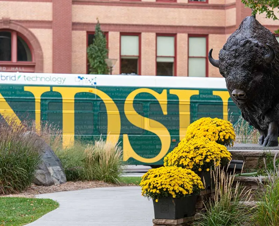 Campus bus passes behind Bison statue.