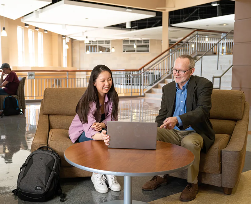 Student showing laptop to instructor in Barry Hall study area.