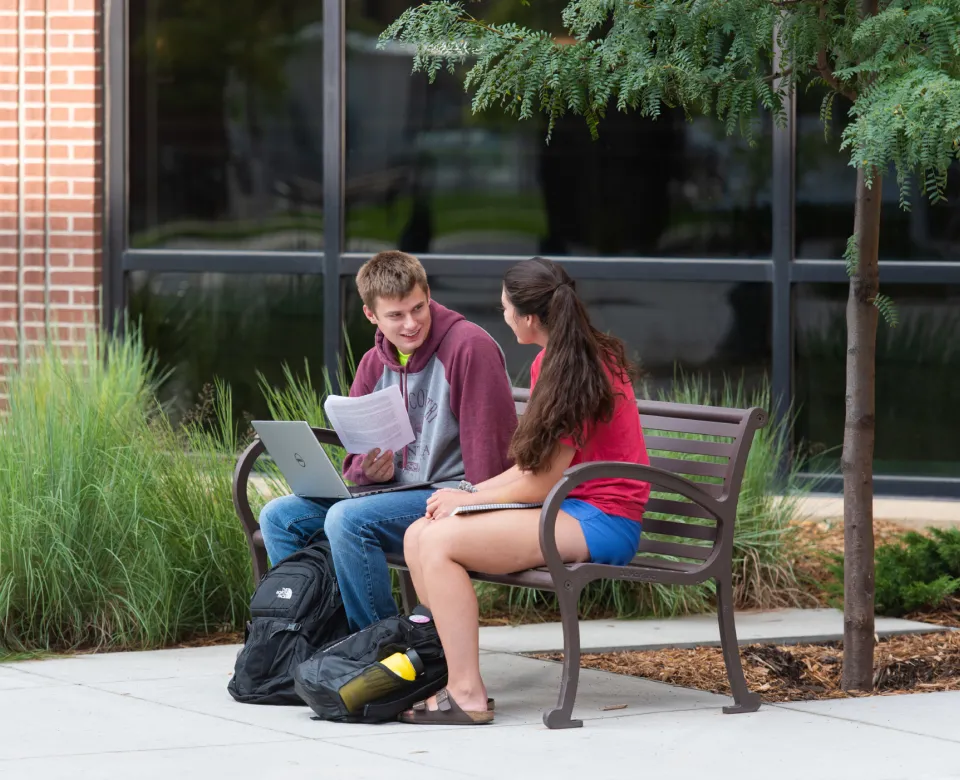 Two students sitting on bench talking.