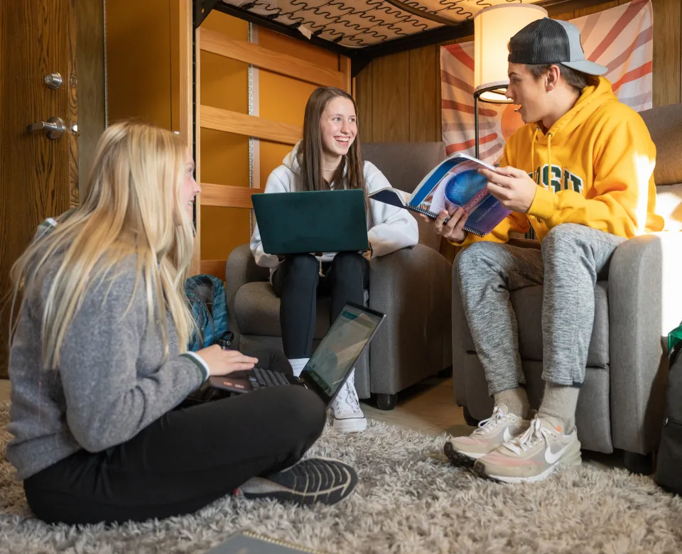 2 female students and one male student talking while sitting in chairs and on floor