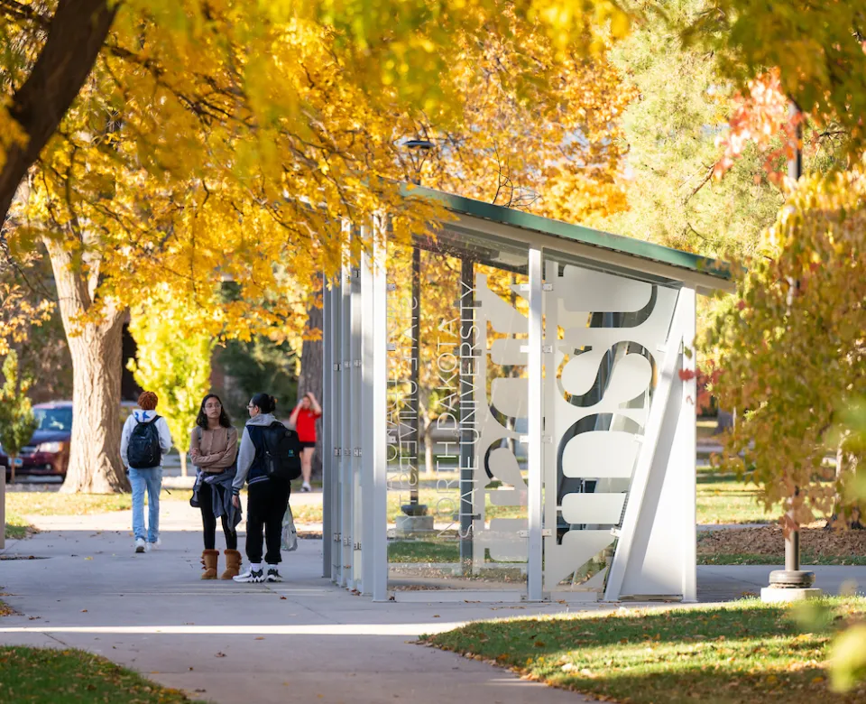 students waiting by bus shelter on campus on a fall day