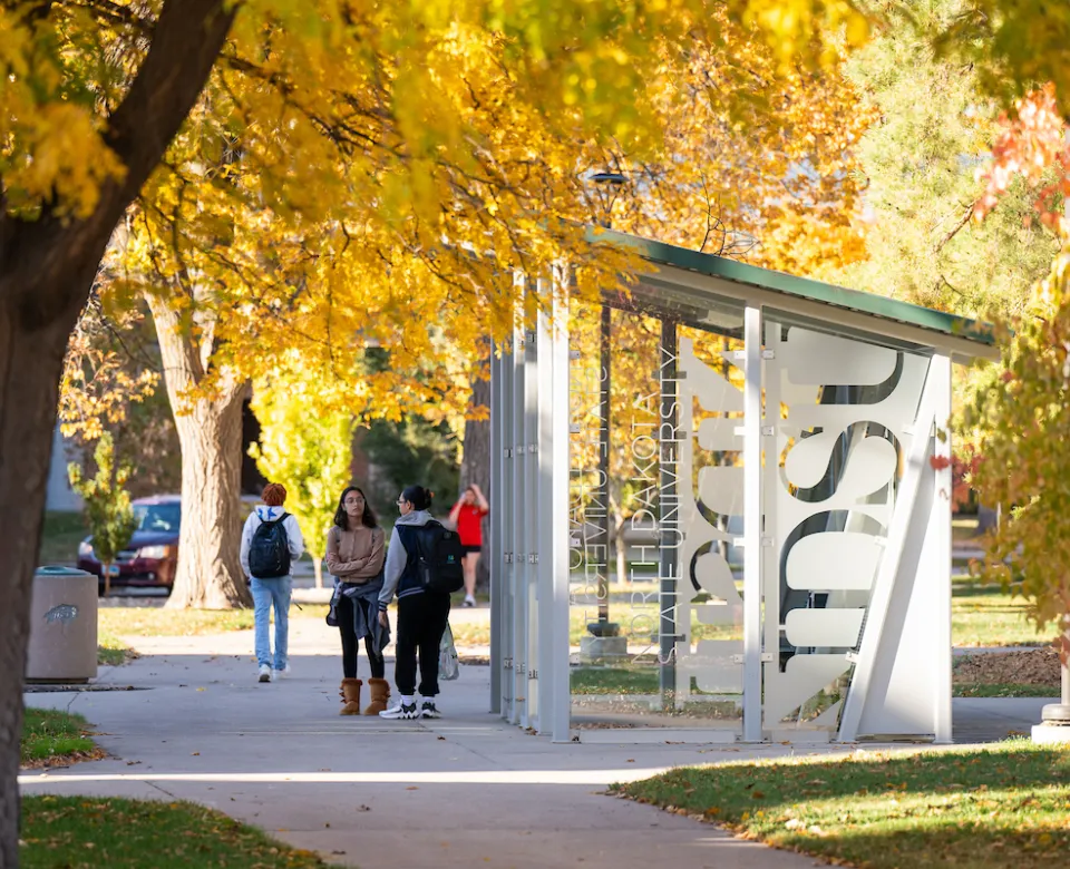 students waiting by bus shelter on campus on a fall day