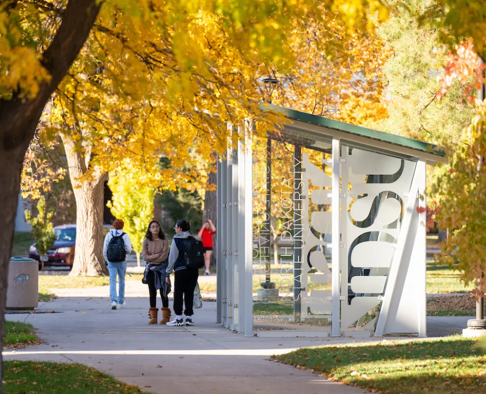students waiting by bus shelter on campus on a fall day