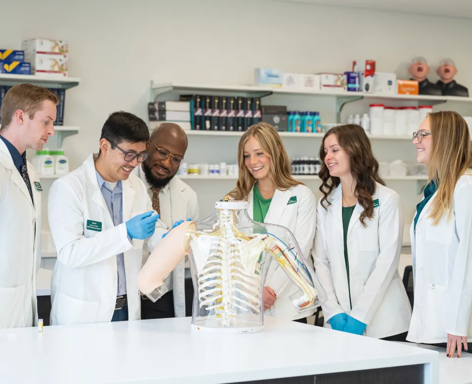 Pharmacy students in a lab observing a student administering a shot to a dummy arm