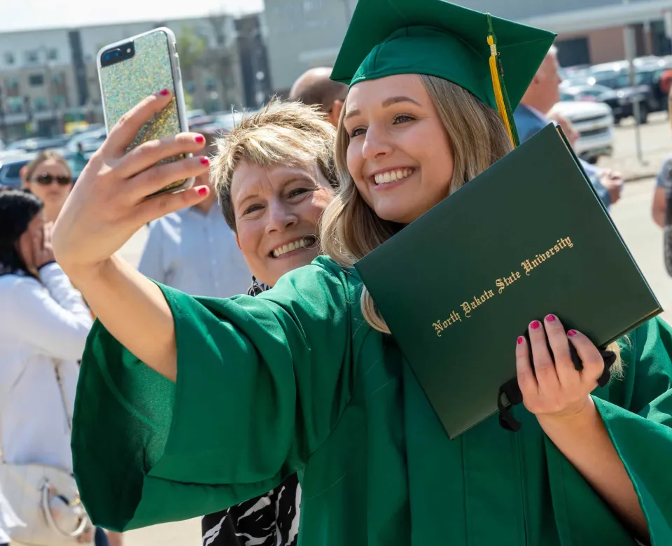 Student in graduation gown with family taking a selfie.