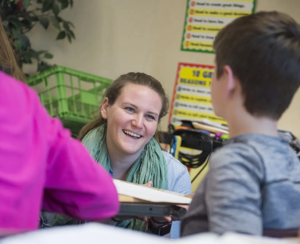 Teacher working with students at desk.