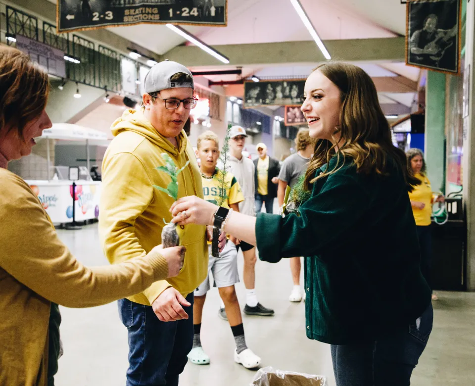 A woman hands a tree seedling to another person