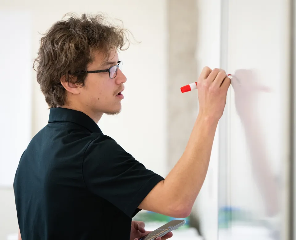 student writing on white board in classroom