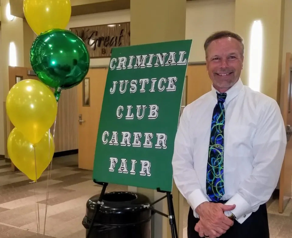 Kevin standing in front of the green criminal justic club career fair signage with yellow and green balloons.