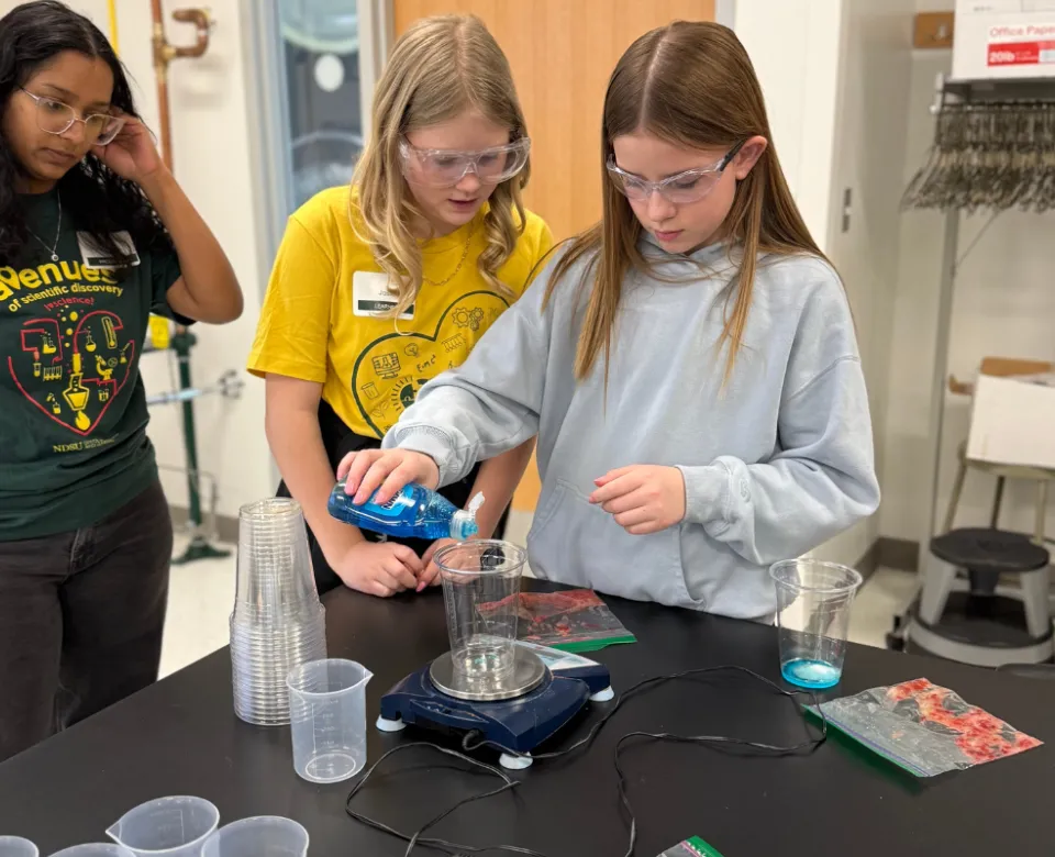 two young girls mixing liquid soap into a beaker at STEM event
