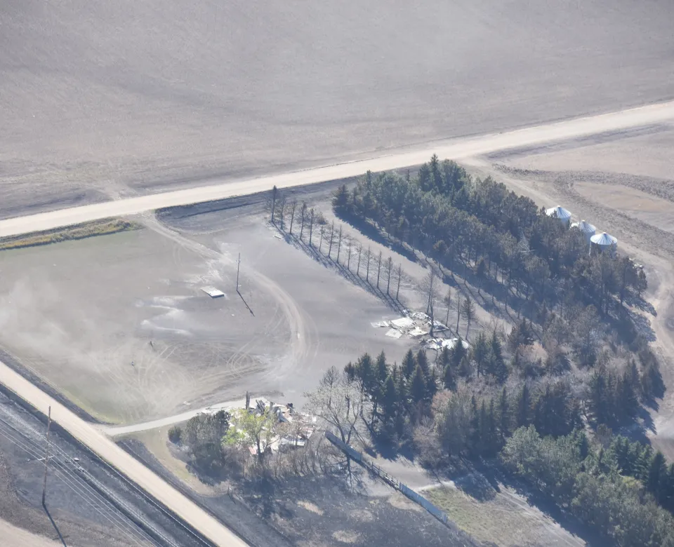 A farmstead showing burnt grass and a burnt row of trees