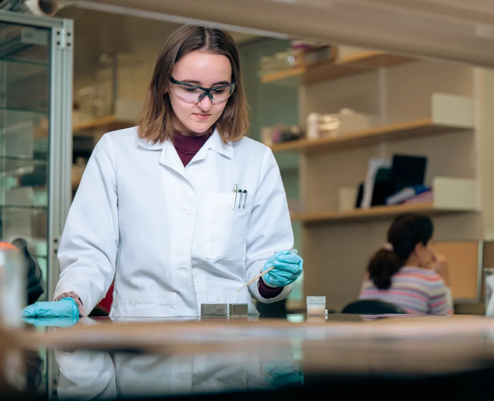 Research student wearing white lab coat and green gloves while working in the lab.