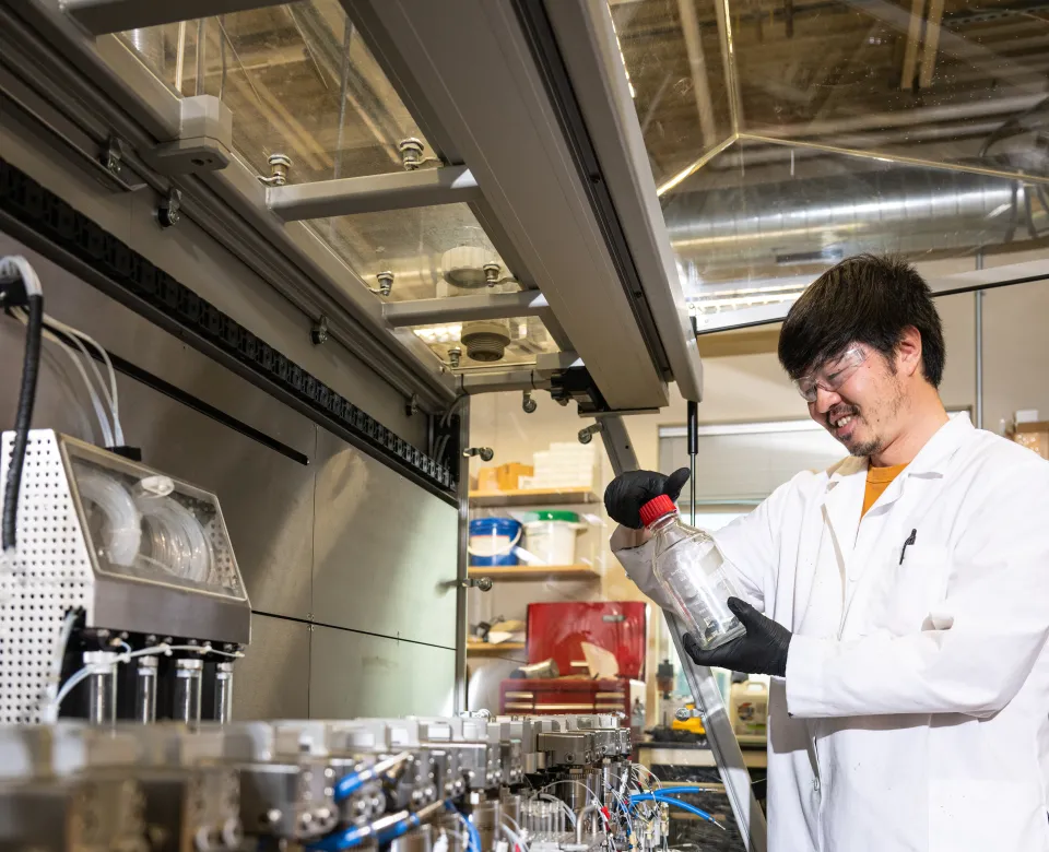 Student wearing a white lab coat and black gloves while working in the lab.