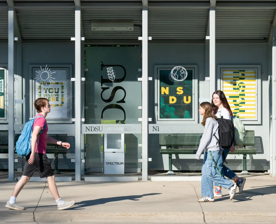 three students walking in front of bus stop on campus