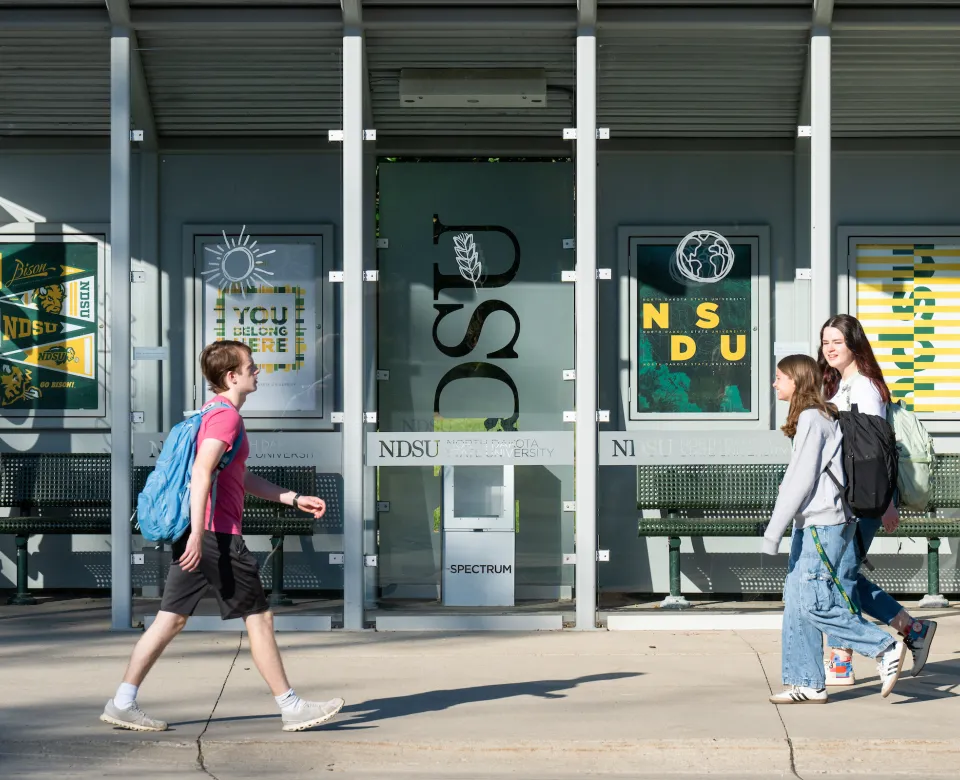 three students walking in front of bus stop on campus