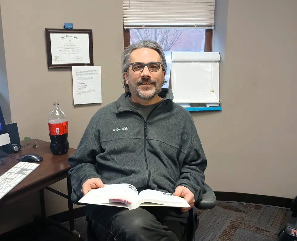 Dr. Robinson sitting in his office with a textbook on his lap