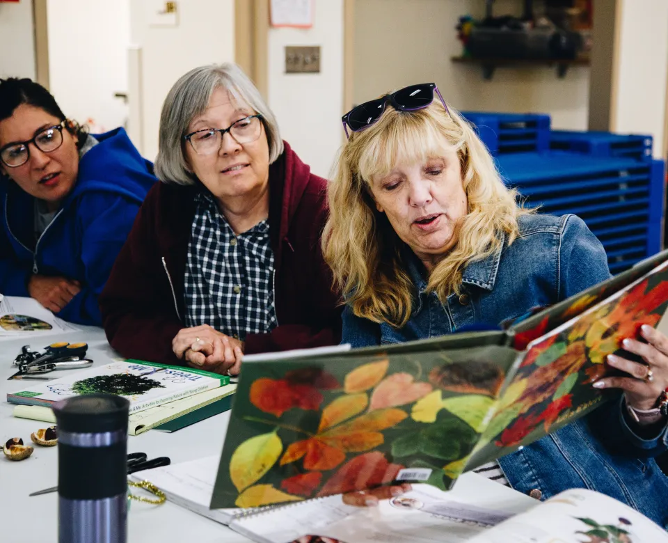 Three women read a book about leaves together