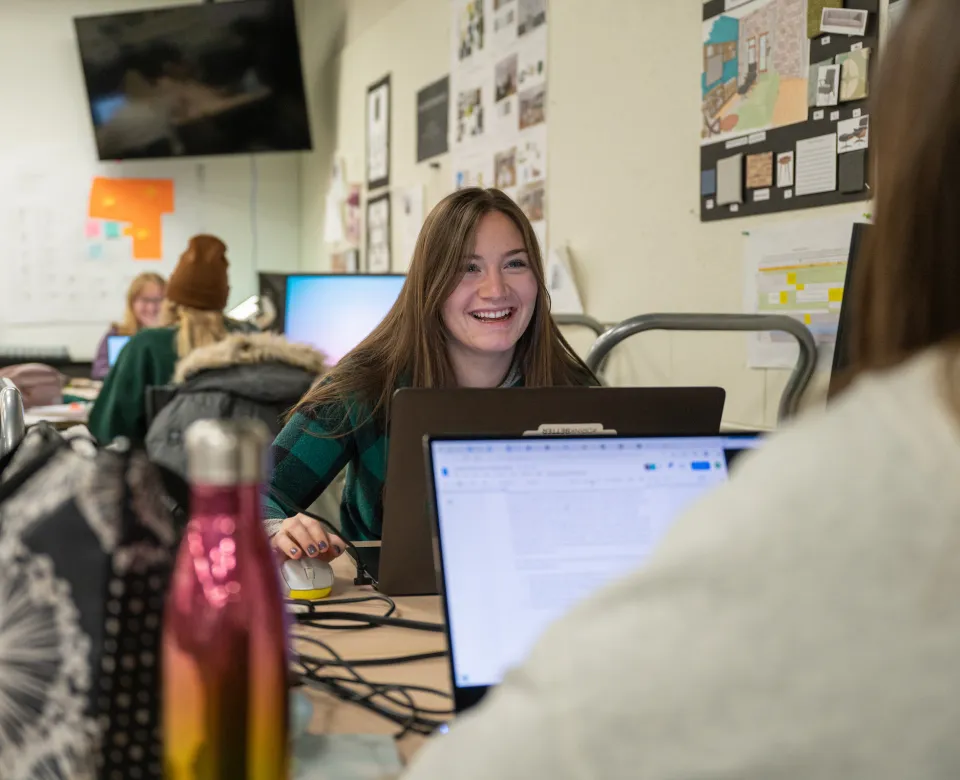 Student working in classroom on laptop with fellow students.