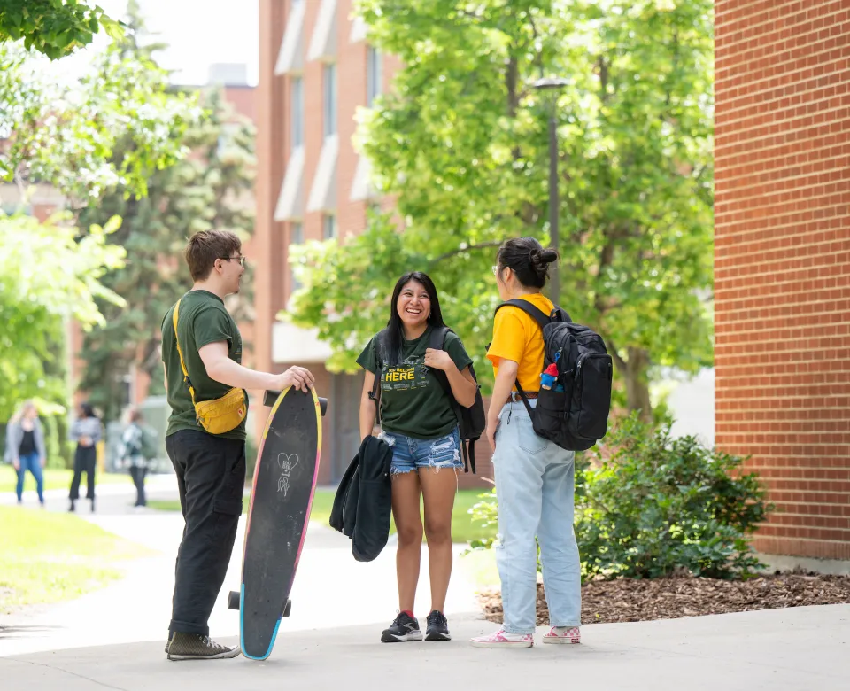 Three students standing outside of residence hall on a sunny day.
