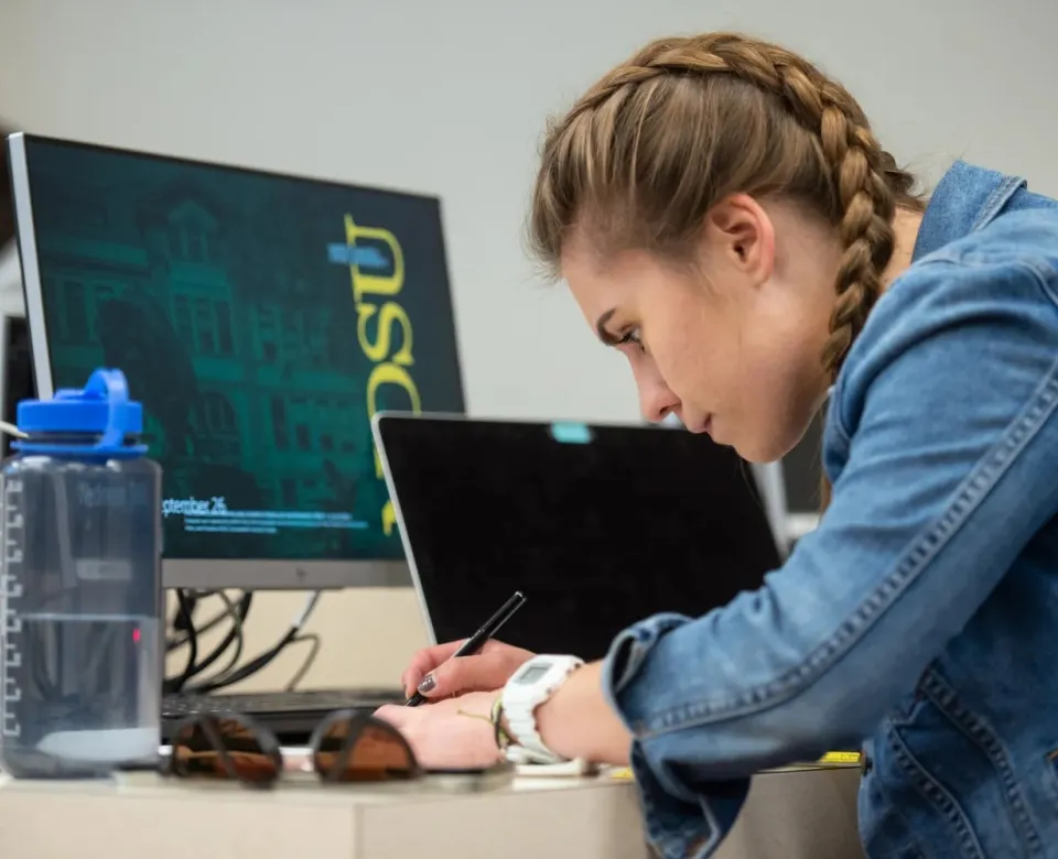 Student reviewing notes while sitting at desk in computer lab.