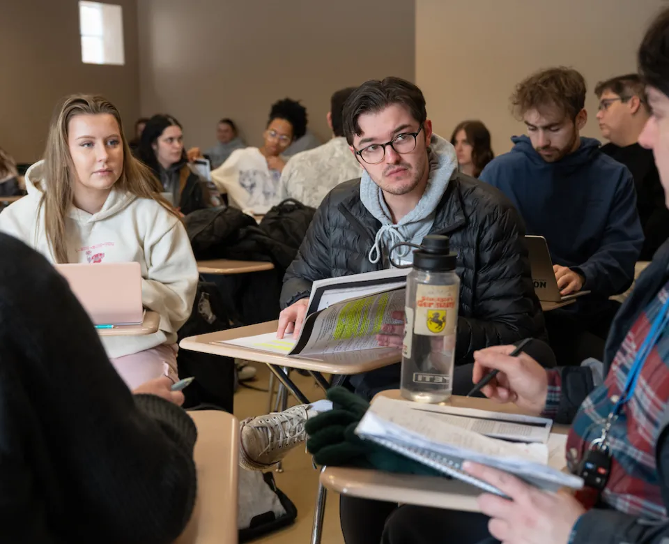 Students sitting at desks located in classroom having a conversation.