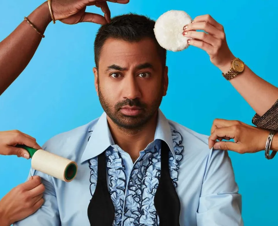 Kal Penn staring at camera with hands putting on make-up, fixing his hair, and straightening his shirt