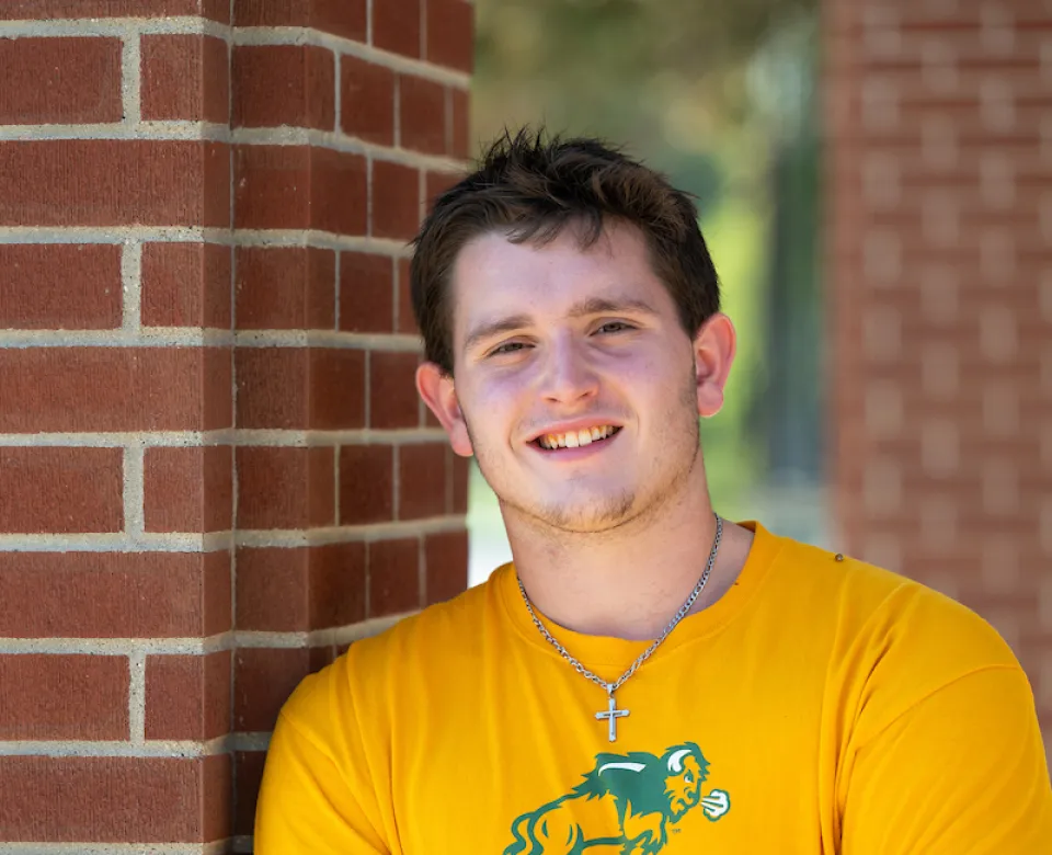 Dawson wearing a yellow NDSU t-shirt while smiling confidently at camera.