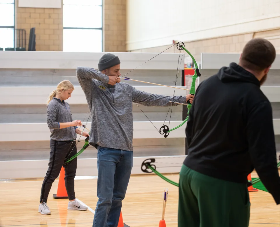 Student working with bow and arrow in gym class.
