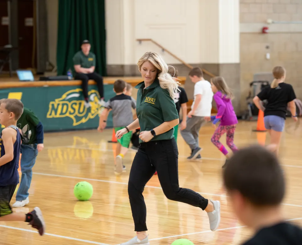 Student running through a gym while teaching a gym class with young students.