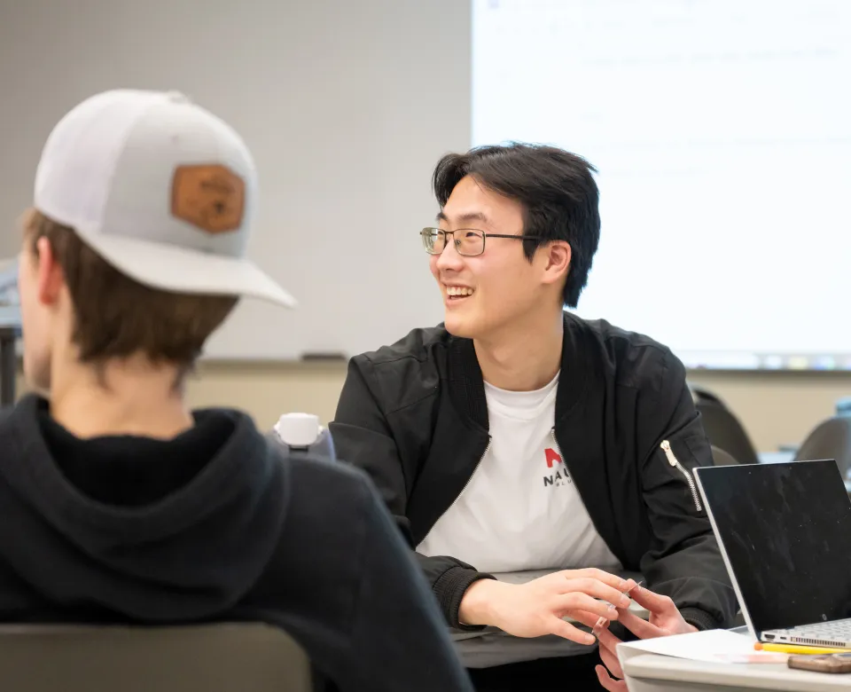 Student sittting at desk smiling while looking to his left.